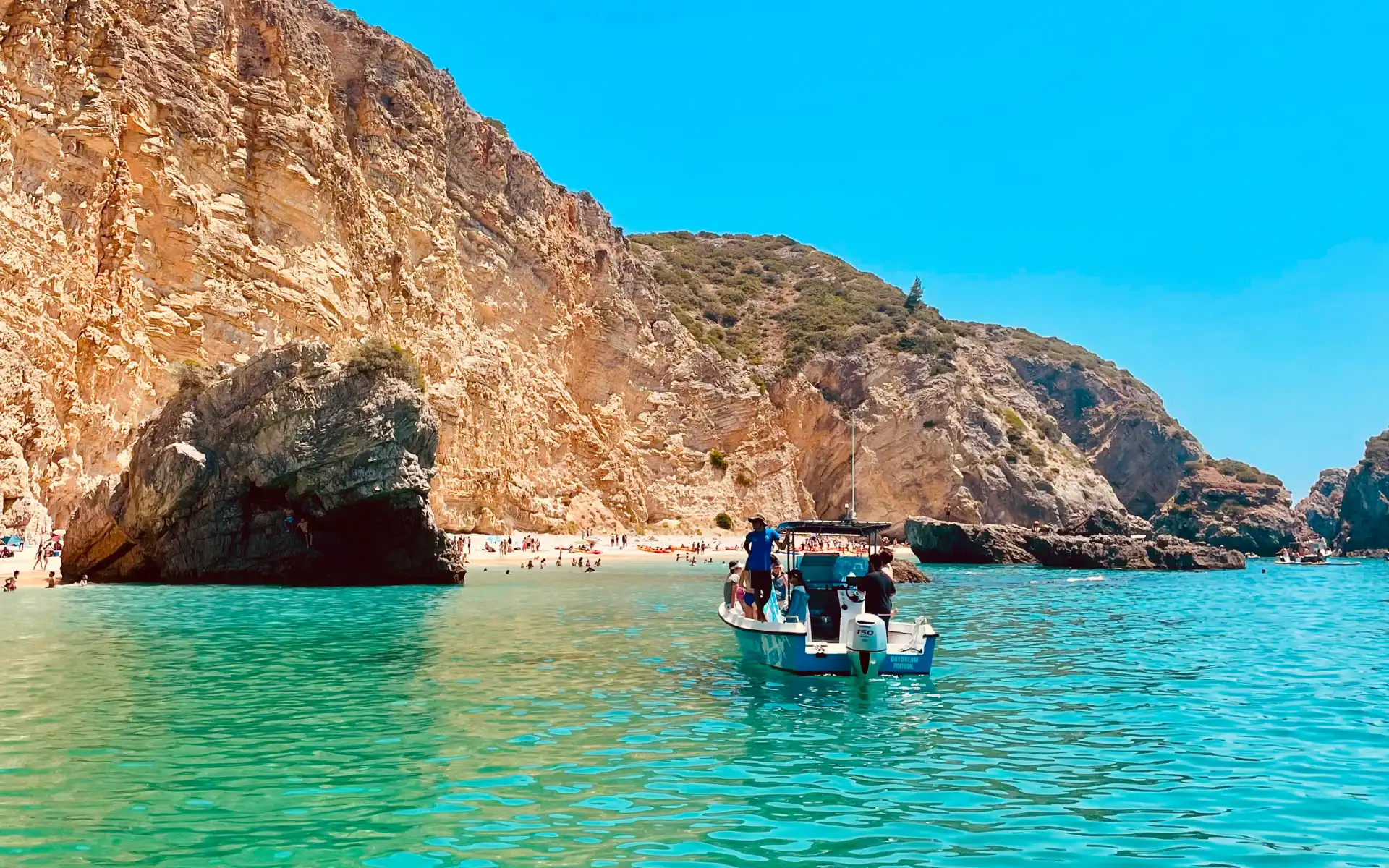 Scenic boat tour approaching a beach filled with visitors, surrounded by dramatic golden cliffs and turquoise waters in Portugal.