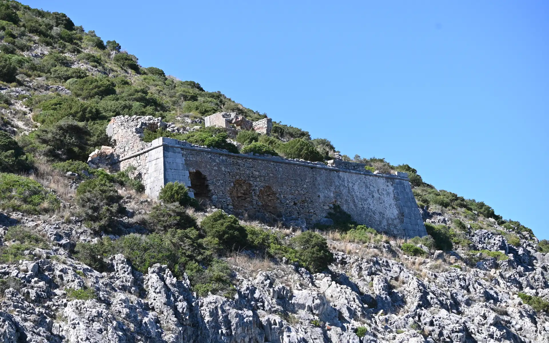 Ancient stone ruins nestled in lush green hills on a sunny day, showcasing Arrábida's blend of nature and history.