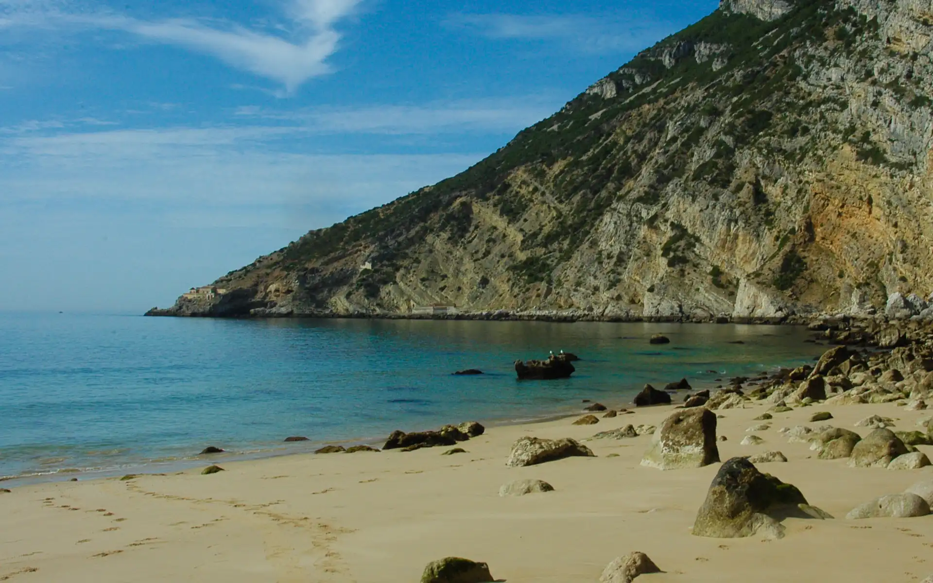 Secluded rocky beach at the base of golden cliffs with crystal-clear turquoise water, a hidden paradise near Lisbon.