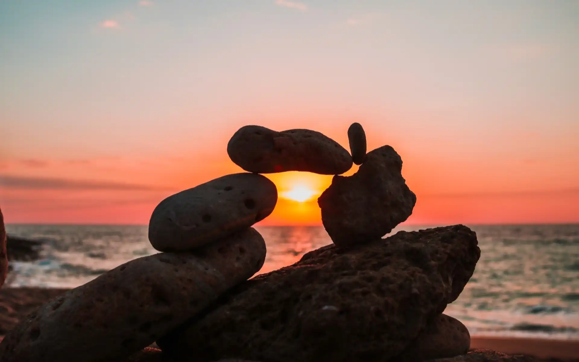 Stack of balanced stones silhouetted against a vibrant orange sunset over the ocean, symbolizing harmony with nature and sustainable tourism.