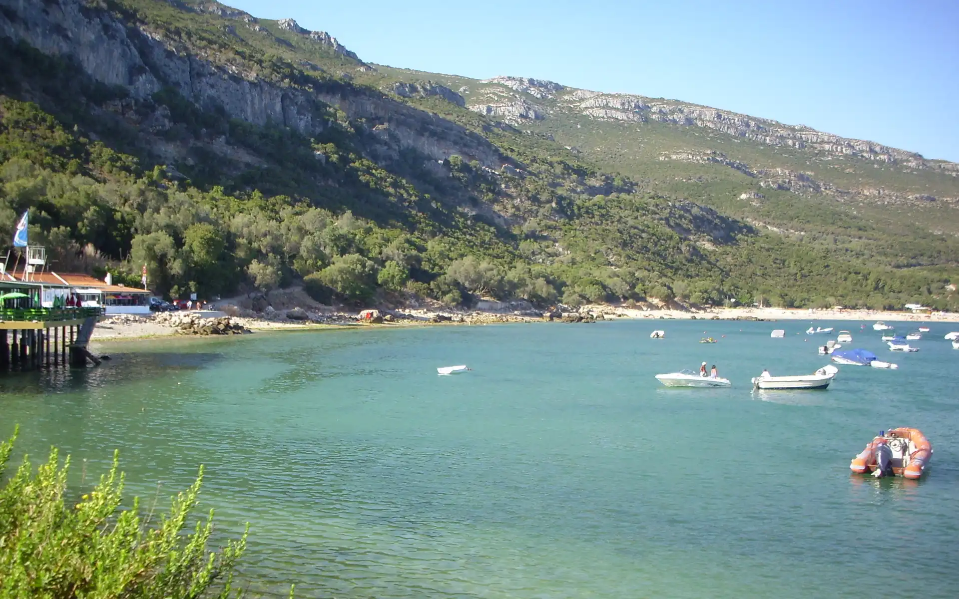 Crystal-clear waters and lush green hills surrounding Portinho da Arrábida Beach, located within the Arrábida Natural Park in Portugal.