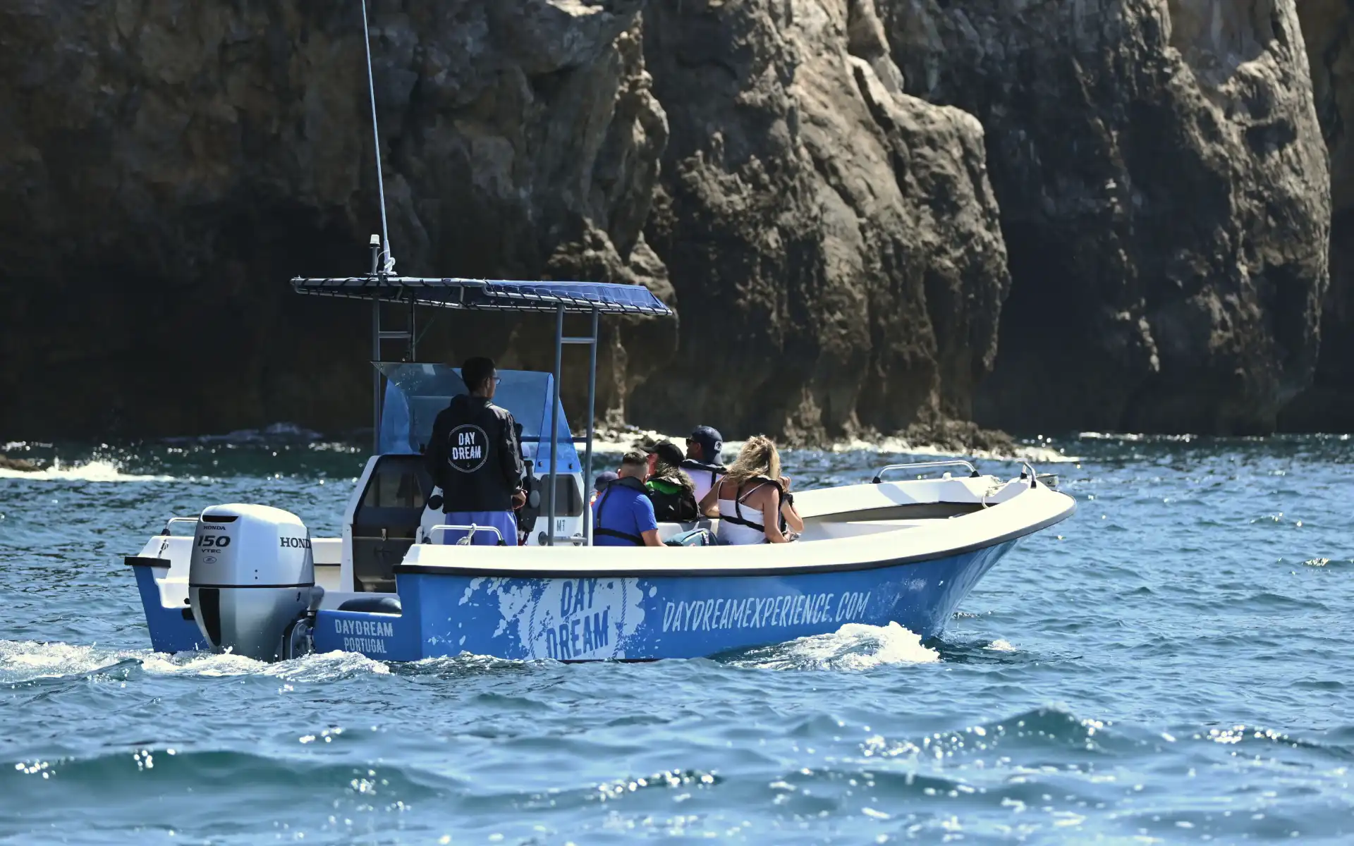 Small tour boat cruising along a rugged cliffside under the summer sun, with passengers enjoying the scenic Portuguese coast.