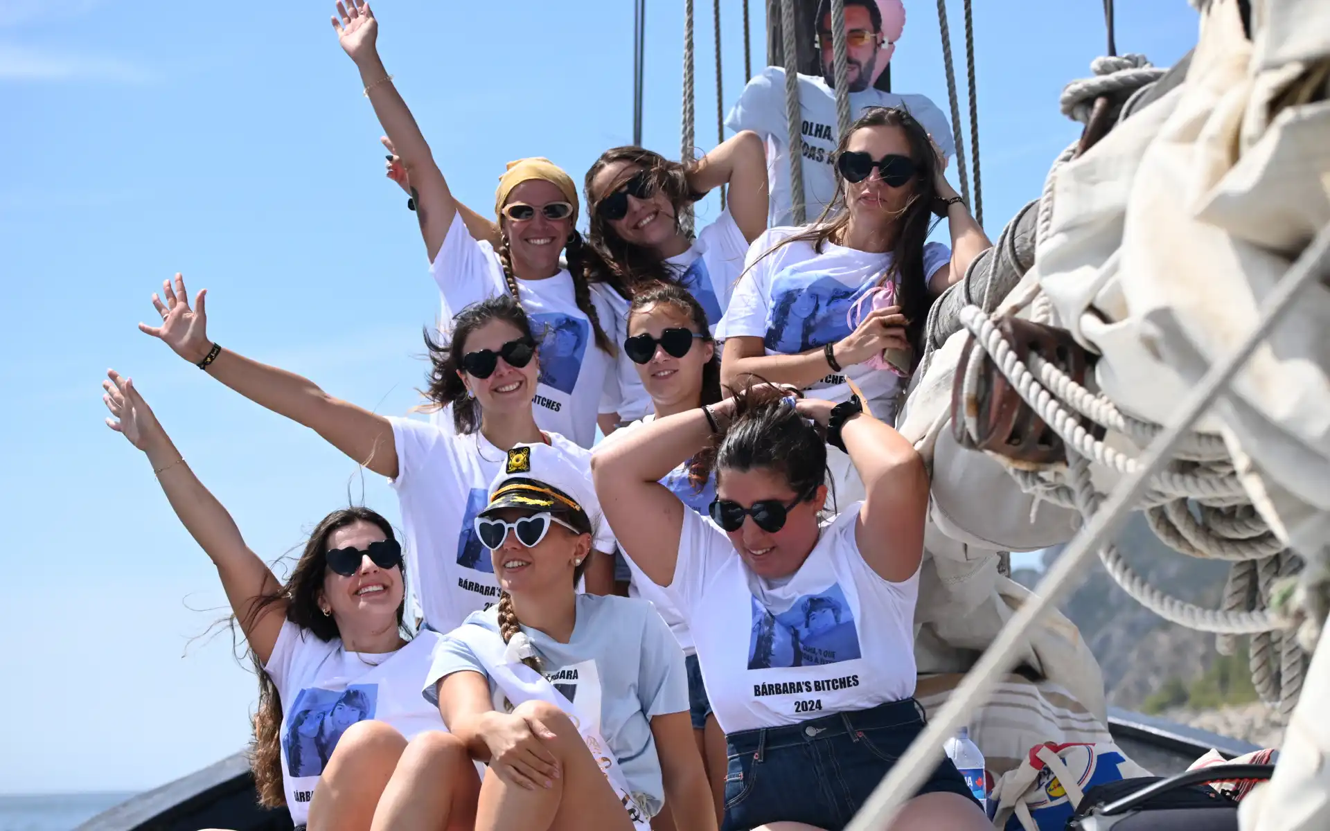 Group of women celebrating a bachelorette party on a boat, wearing matching custom shirts and smiling under a sunny sky.